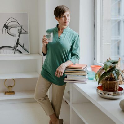 Woman Holding a Glass of Water Standing Beside a Window